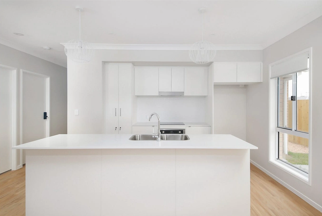 Open-plan kitchen in home at 8 Lilly Lane, Logan featuring white cabinetry and island bench.