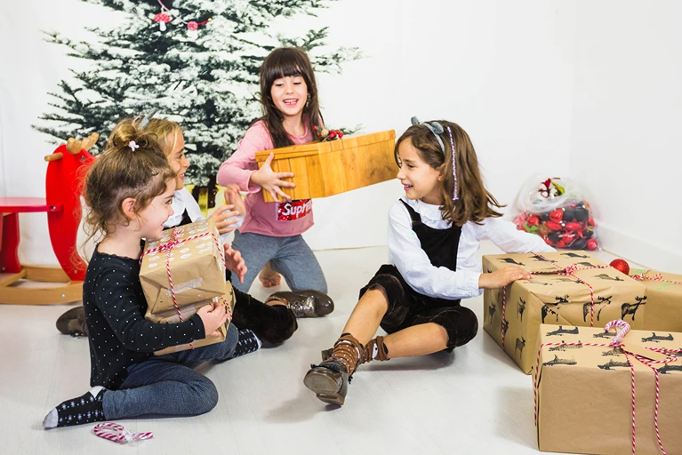 Children enjoying December school holiday activities with gifts and smiles under a Christmas tree