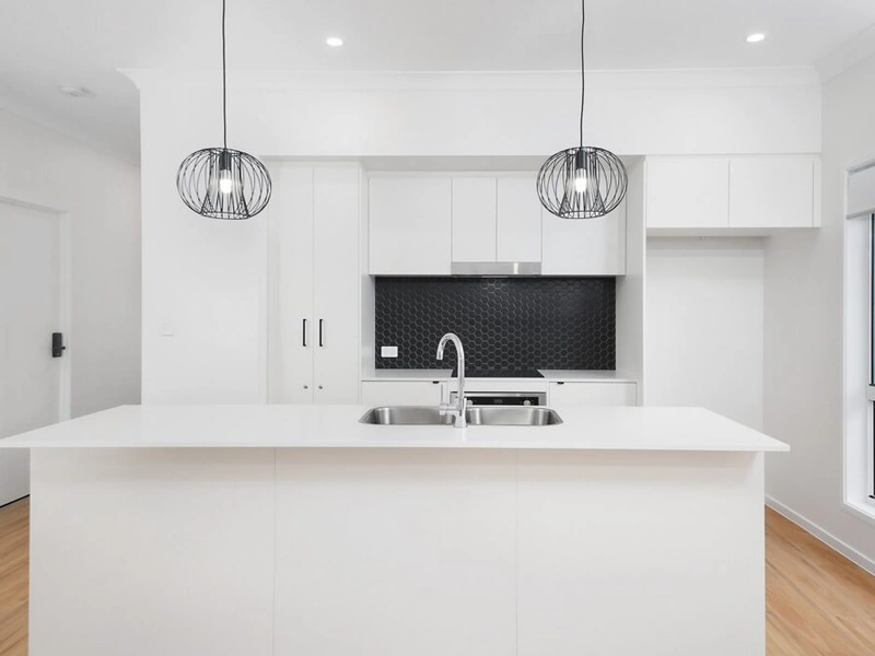 Modern white kitchen with island bench, pendant lights and black splashback at Logan Reserve QLD 4133 property.